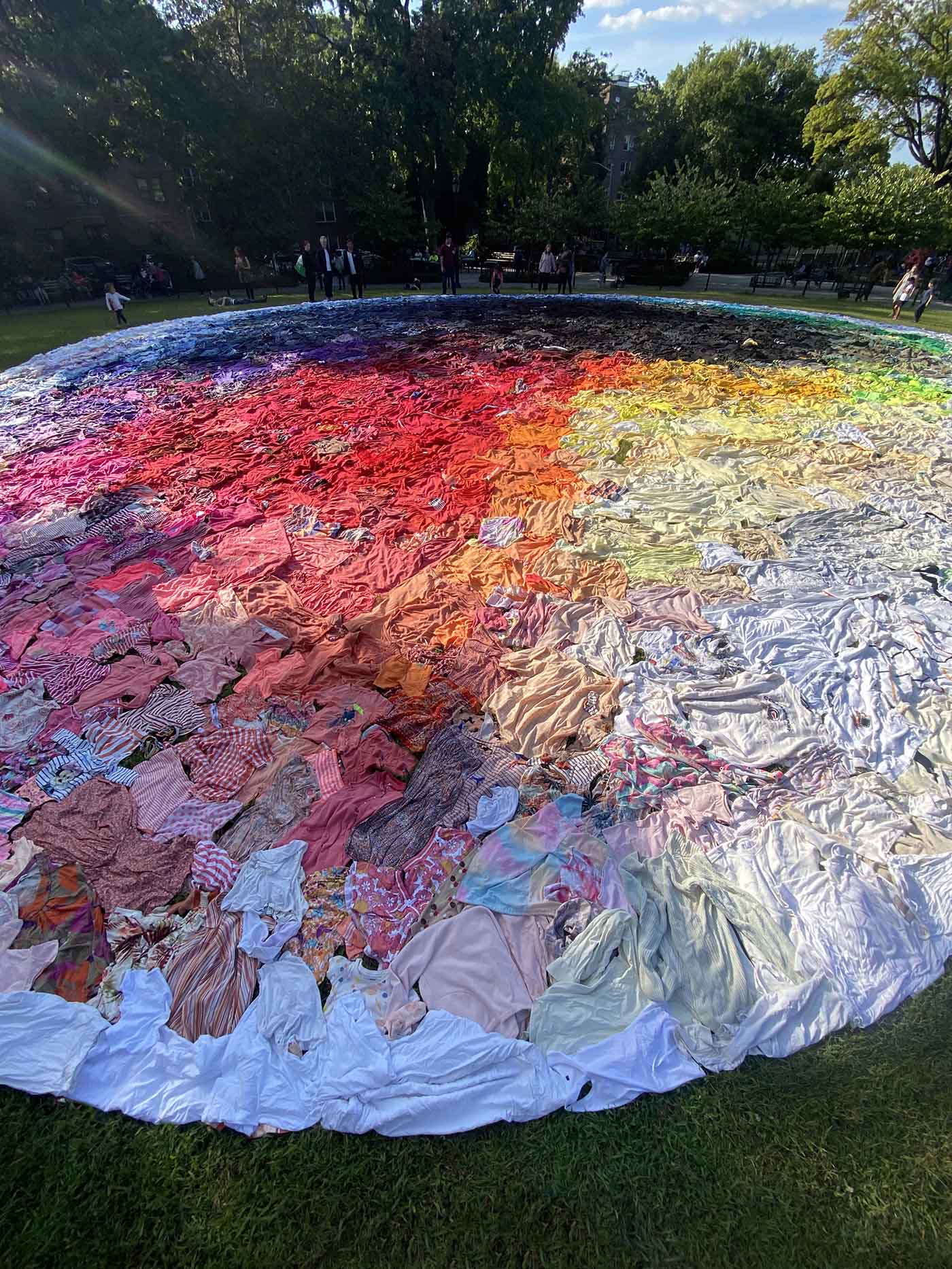 Clothing Sculpture: To Reshuffle the Sun – The hill-shaped lawn in Travers Park covered with second-hand clothing, arranged like a giant color wheel but with a dark center and a light outer edge. 100 feet wide.